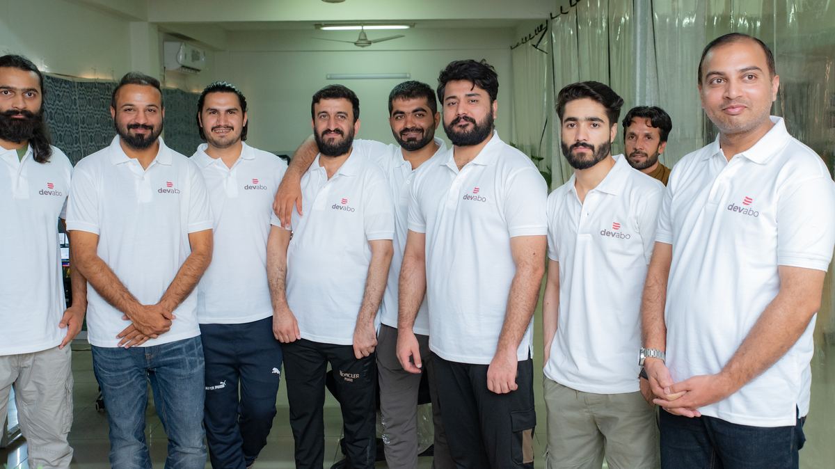 Rund ein Dutzend Entwickler in weißen DevAbo-Poloshirts stehen lächelnd im Büro in Islamabad.